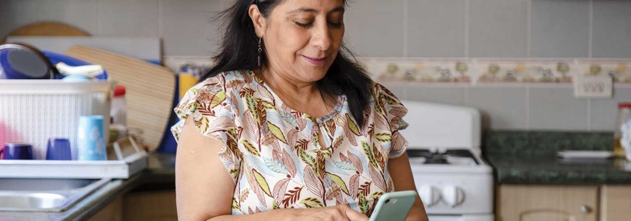 Hispanic mom searching recipes on her phone-mature woman preparing healthy and organic salad while checking her cell phone-housewife cooking while she looks at a phone