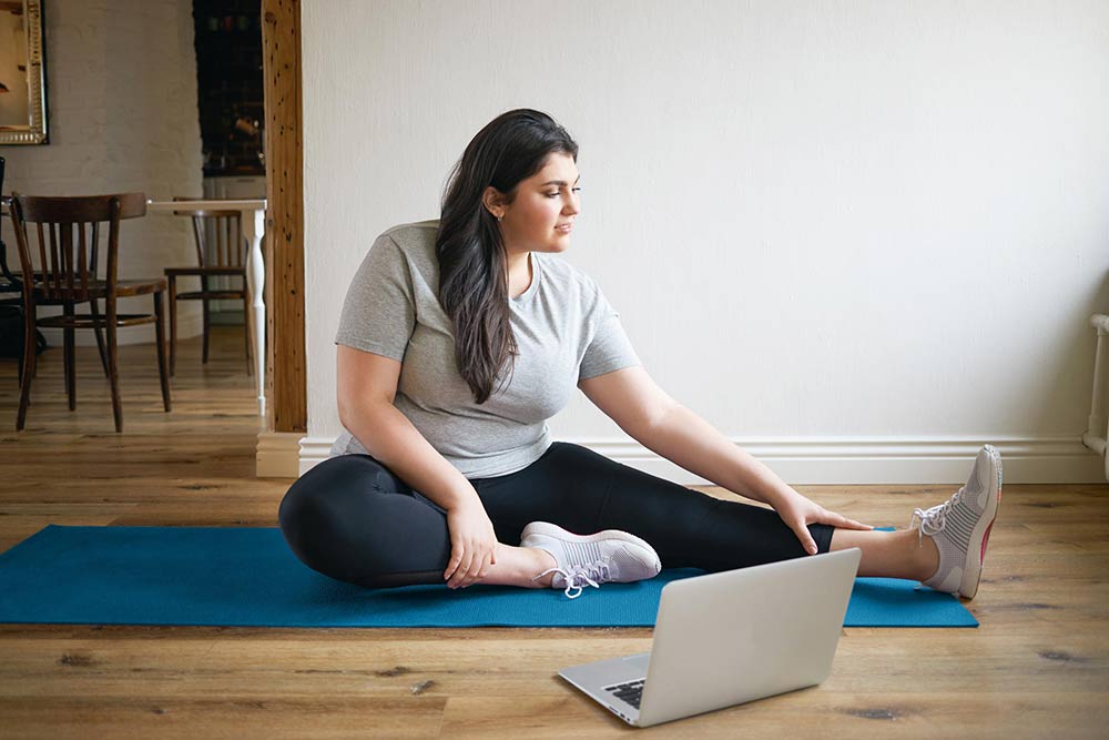 Woman at home doing seated yoga stretches on a mat.