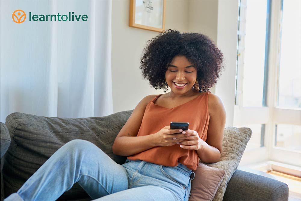 A smiling woman sitting on a couch looking at a mobile phone