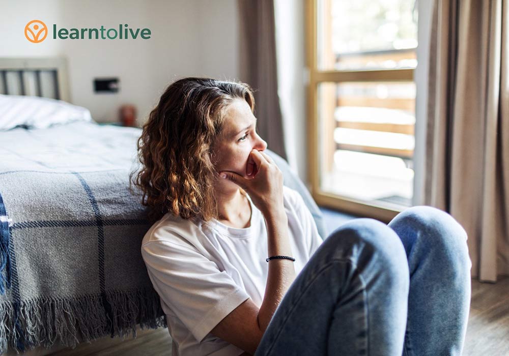 A sad-looking woman sitting on the floor of a bedroom