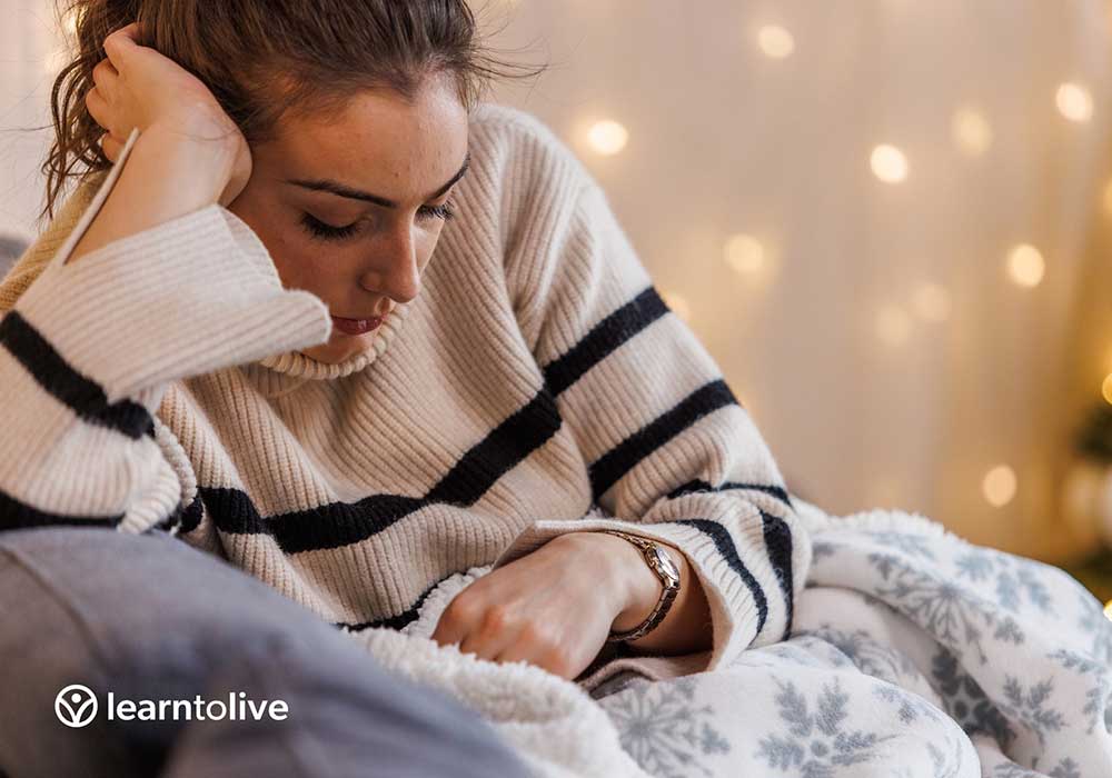 Depressed woman sitting on couch with blanket
