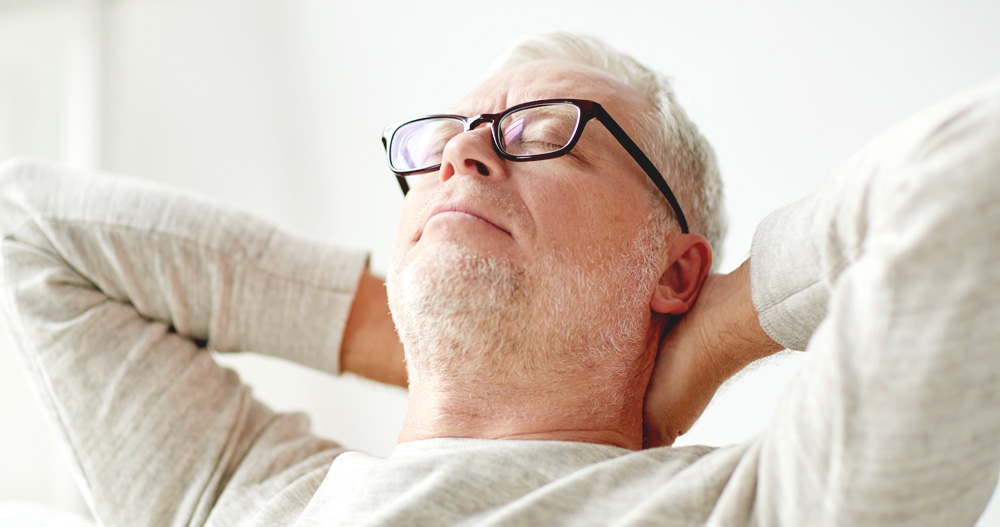 Elderly man relaxing with eyes closed and leaning back with hands behind his head