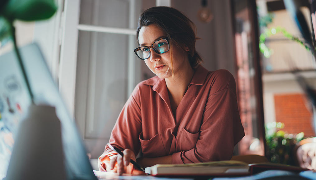 Woman looking at a laptop and writing notes